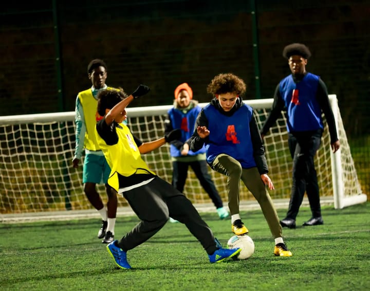 Young footballers playing five-a-side on floodlit pitch