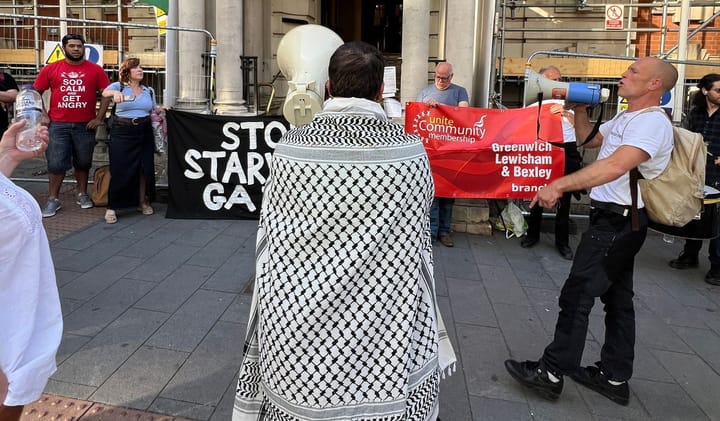 Campaigner in keffiyeh outside Woolwich Town Hall, banners read Stop Starving Gaza and Unite community.