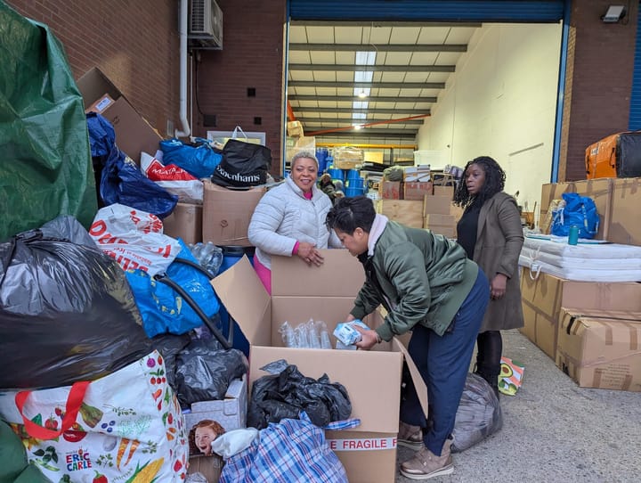 Piles of bags and boxes, 3 volunteers sort and pack donations at Kingsley Shipping. 