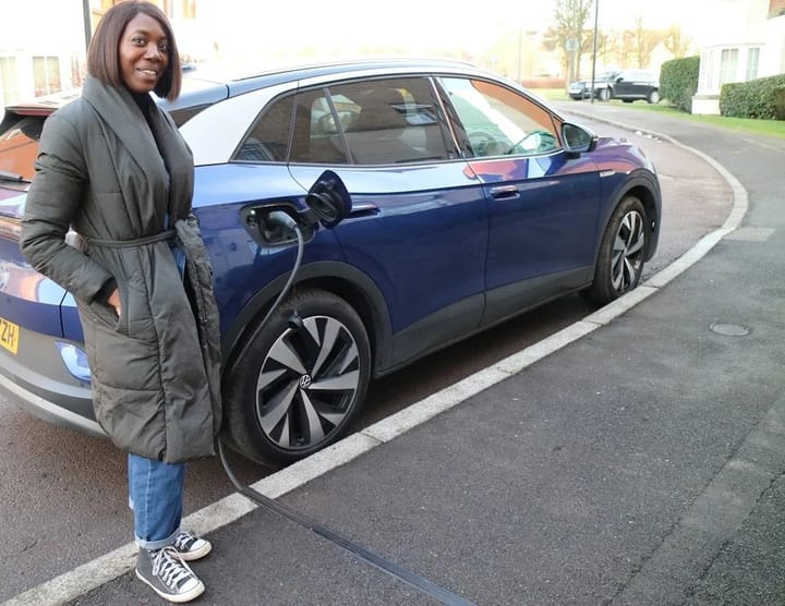 Smiling woman standing next to car which is charging with cross-pavement charging cable embedded in pavement. 