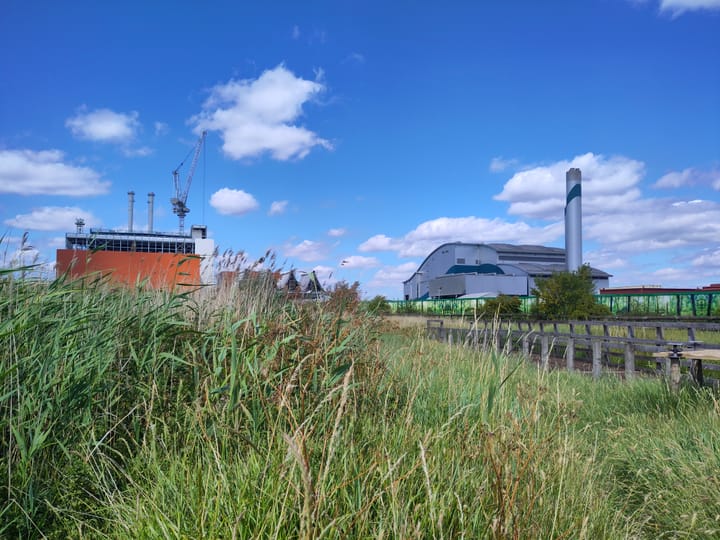 2 incinerators with tall chimneys seen through long grass on reserve, Riverside 2 (in construction) and Riverside 1. 